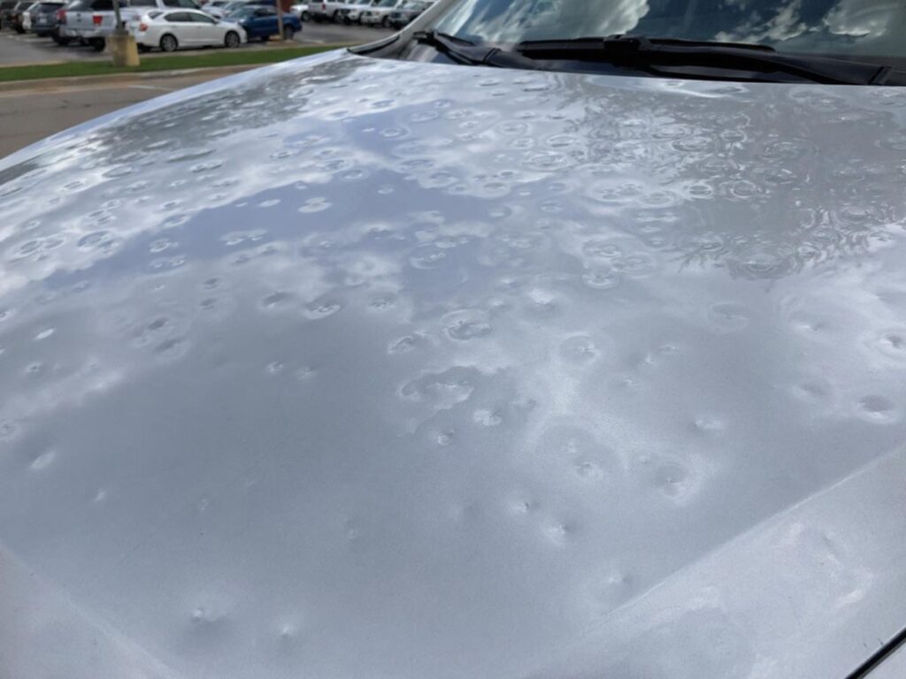 Close-up of multiple hail dents on a vehicle hood after a Wisconsin hail storm.