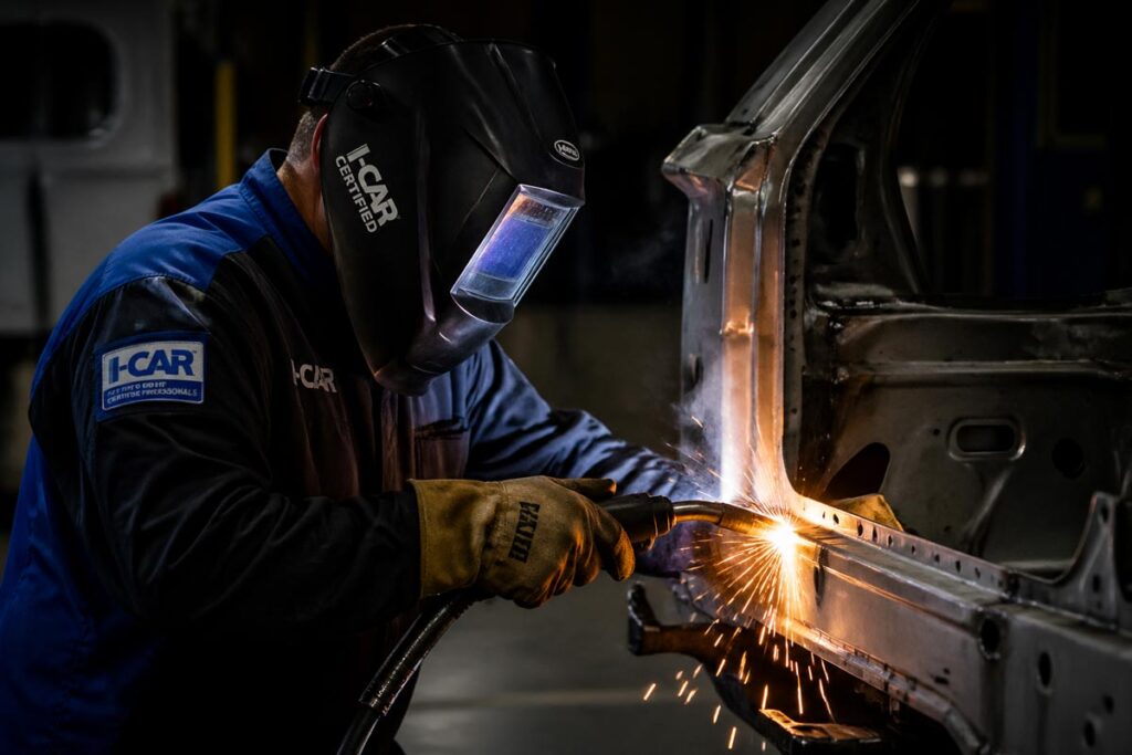 I-CAR certified collision technician performing structural welding on a vehicle frame in a professional auto body shop.