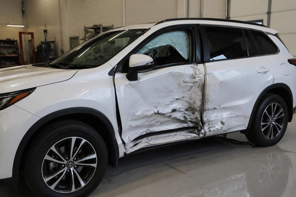 Vehicle showing side-impact T-bone collision damage on driver door and B-pillar in repair shop.